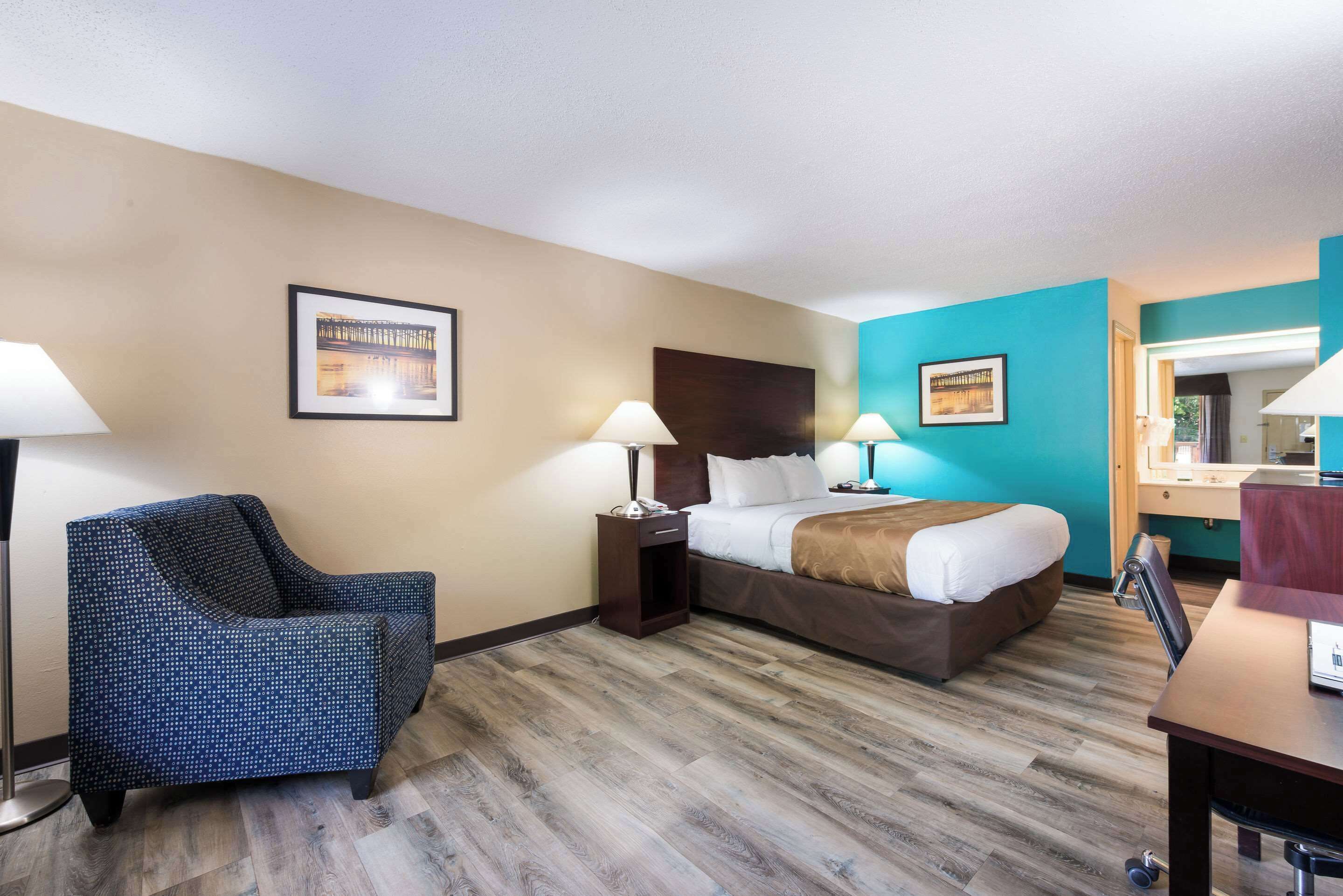 A hotel room with a bed, two bedside tables with lamps, a chair, and a desk.