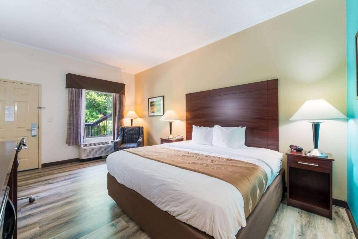 Ein Hotelzimmer mit einem großen Bett, zwei Nachttischlampen, einem Sessel, einem Fenster mit Vorhängen und einer Tür.