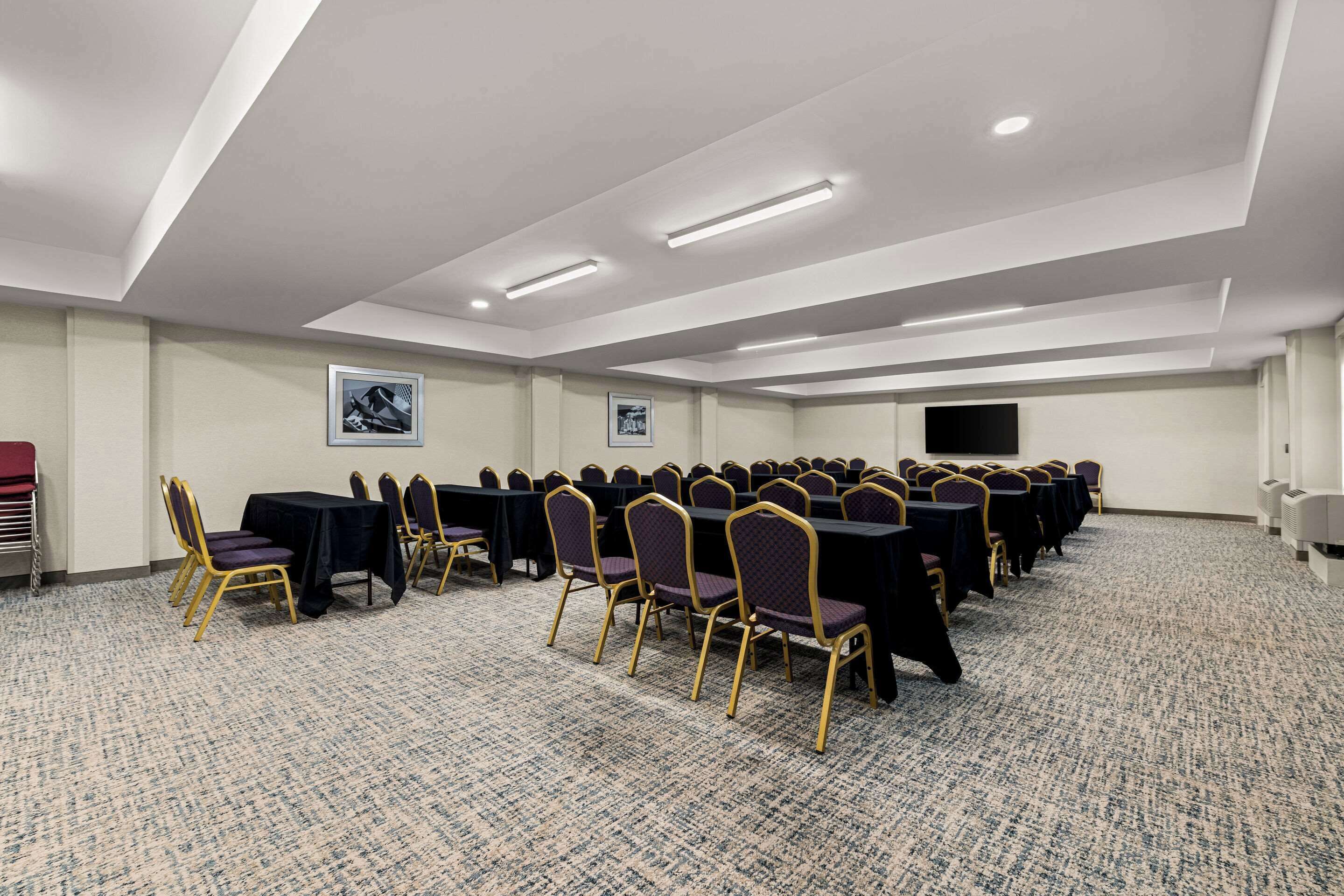 A conference room with rows of tables and chairs, recessed lighting, and a carpeted floor.