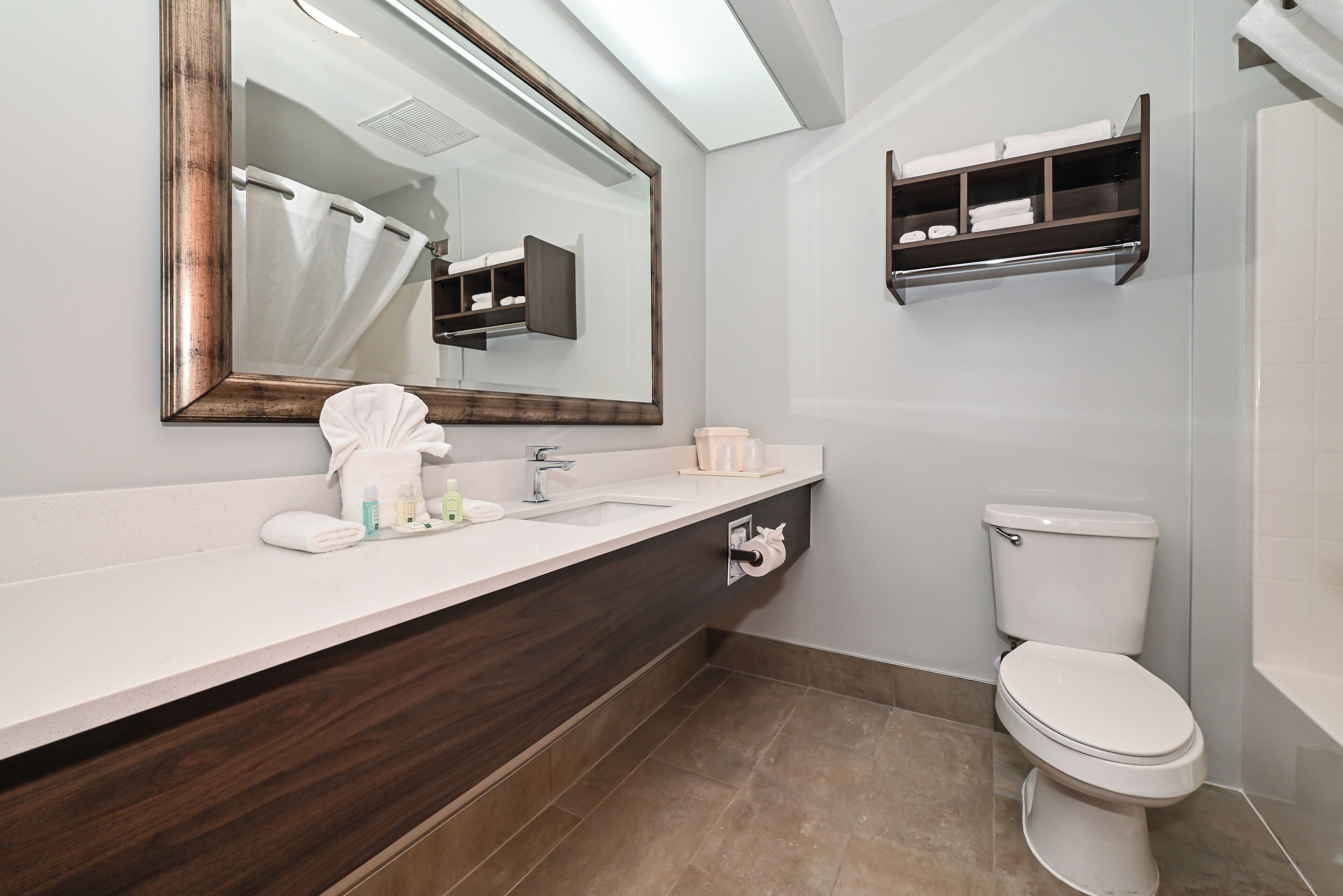 A modern bathroom with a large mirror, a white sink, a dark wood vanity, a toilet, and a towel rack.