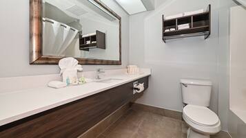 A modern bathroom with a large mirror, a white sink, a dark wood vanity, a toilet, and a towel rack.