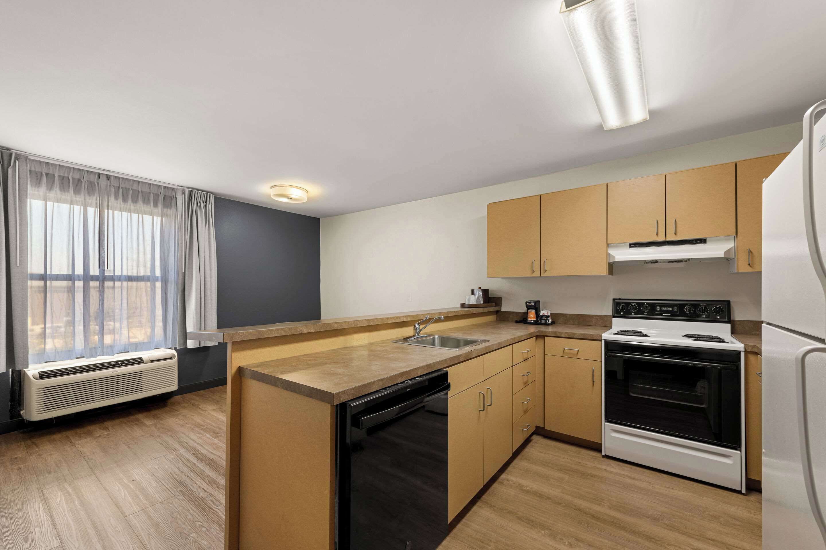 A modern kitchen with a dishwasher, stove, and sink. There is a window with curtains and an air conditioning unit.