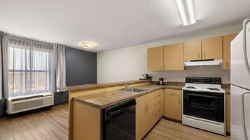 A modern kitchen with a dishwasher, stove, and sink. There is a window with curtains and an air conditioning unit.