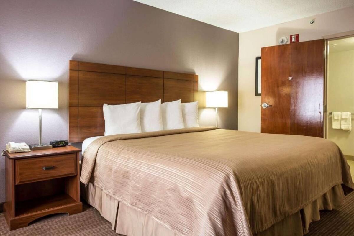 Una habitación de hotel con una cama grande, lámparas de noche, un cabecero de madera, una mesita de noche y un armario.