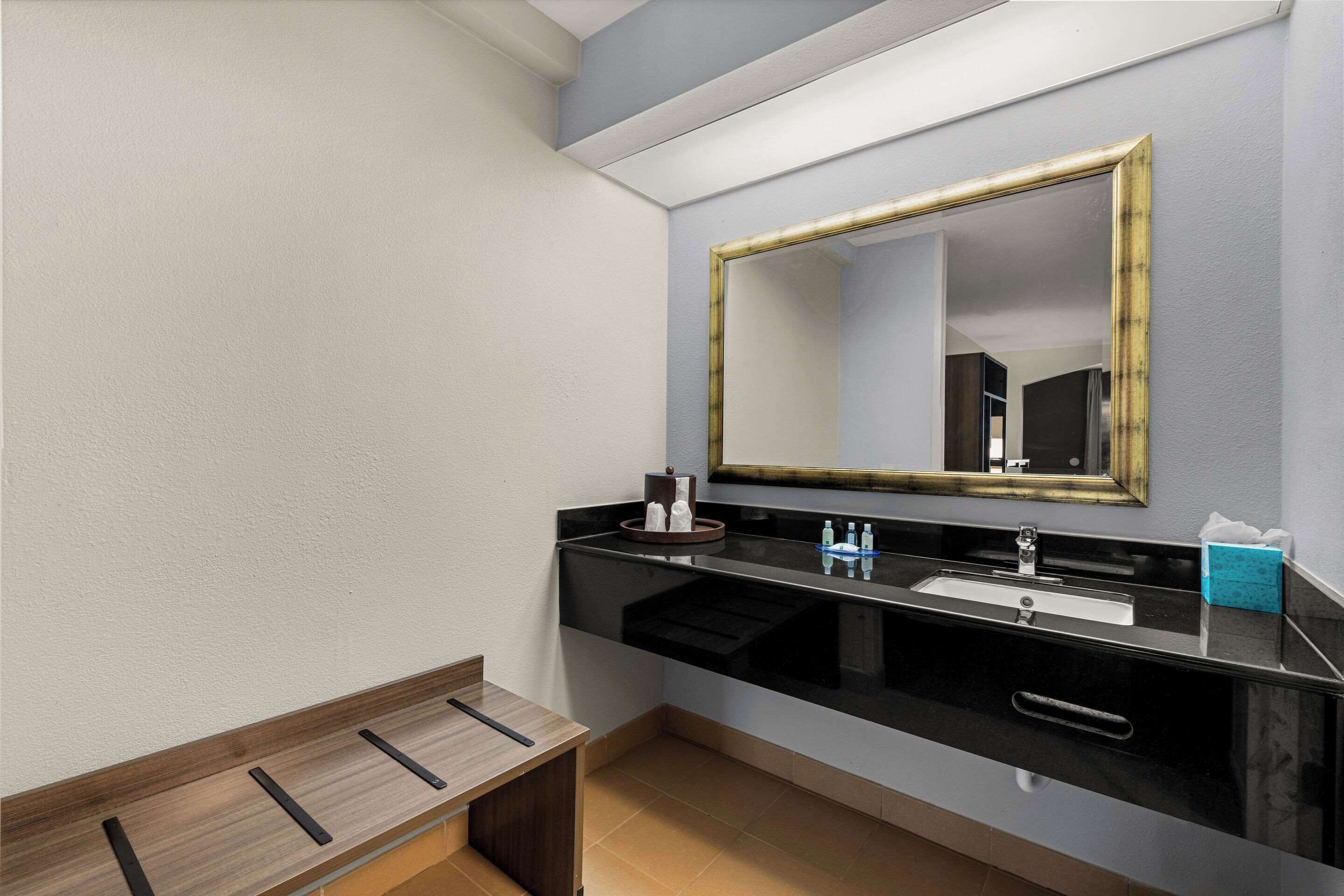 Un baño moderno con un lavabo negro, un espejo con marco dorado y un banco de madera.