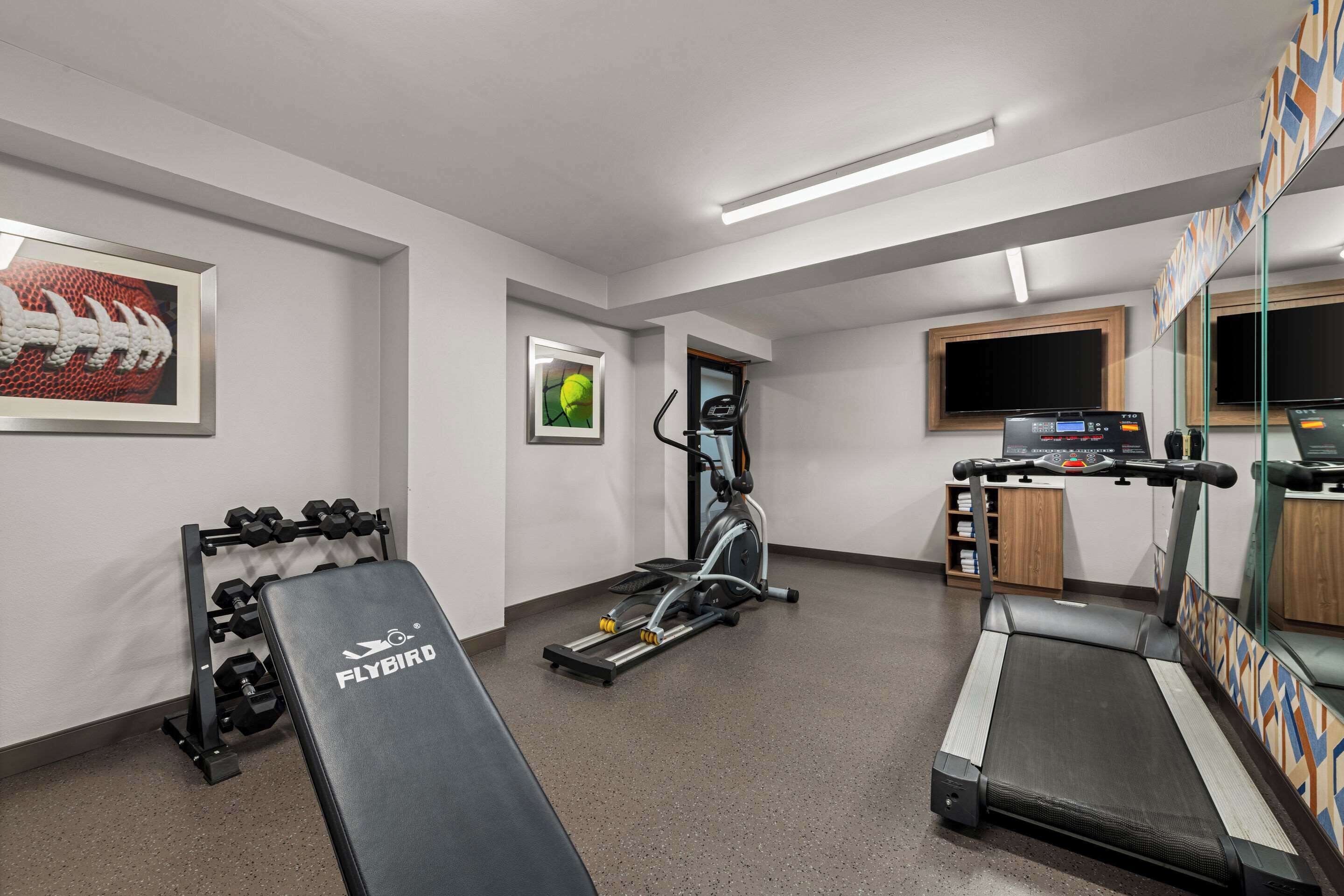 Un gimnasio con cinta de correr, elíptica, mancuernas y banco.