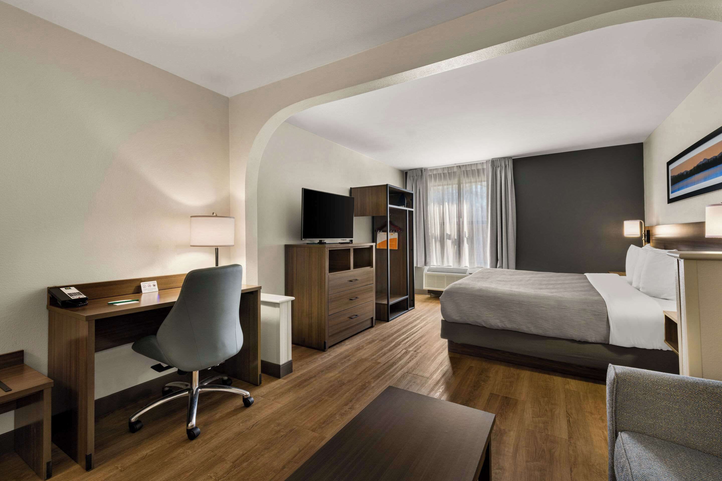 Habitación de hotel con escritorio, silla, cama y televisor.