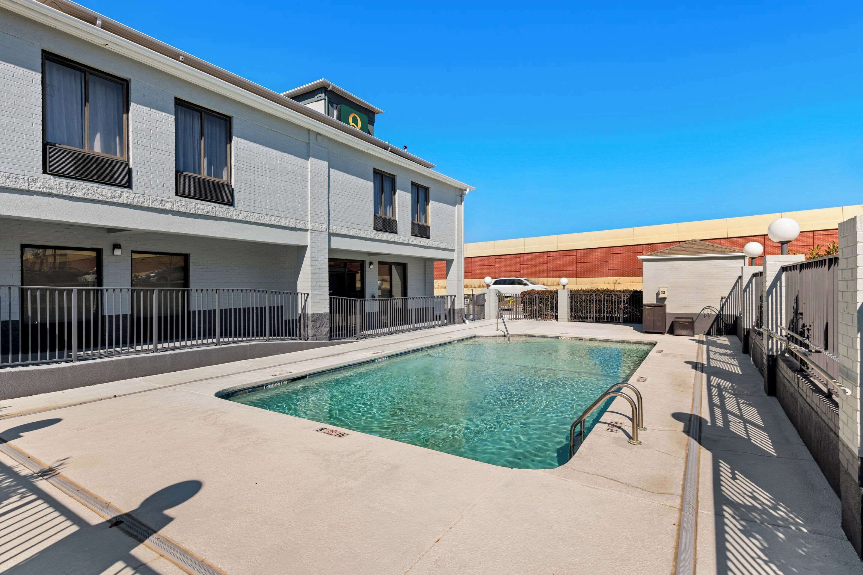 A swimming pool with a clear blue water, surrounded by a concrete deck and a metal fence.