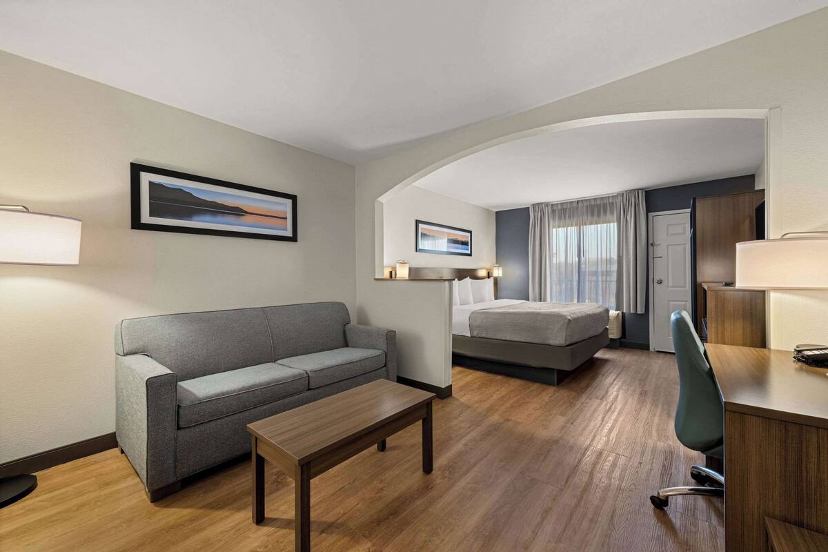 Habitación de hotel con sofá, cama, escritorio y silla. Dos cuadros enmarcados adornan la pared.