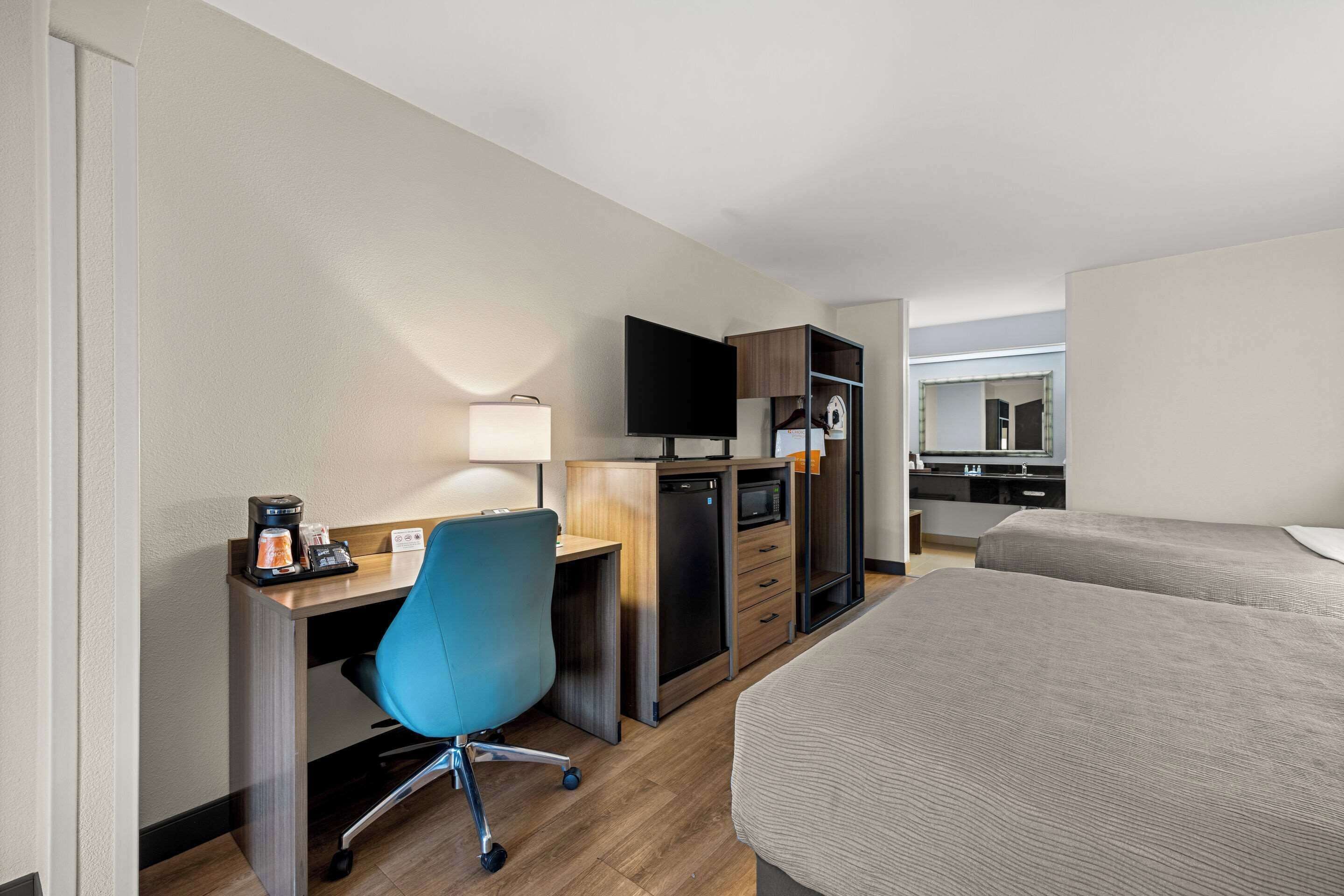 Habitación de hotel con escritorio, silla, televisor, microondas y cama.