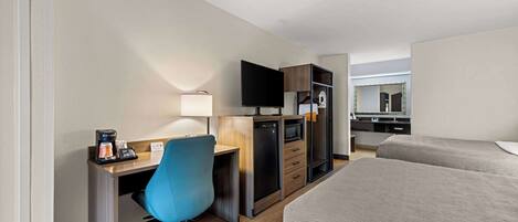 Habitación de hotel con escritorio, silla, televisor, microondas y cama.