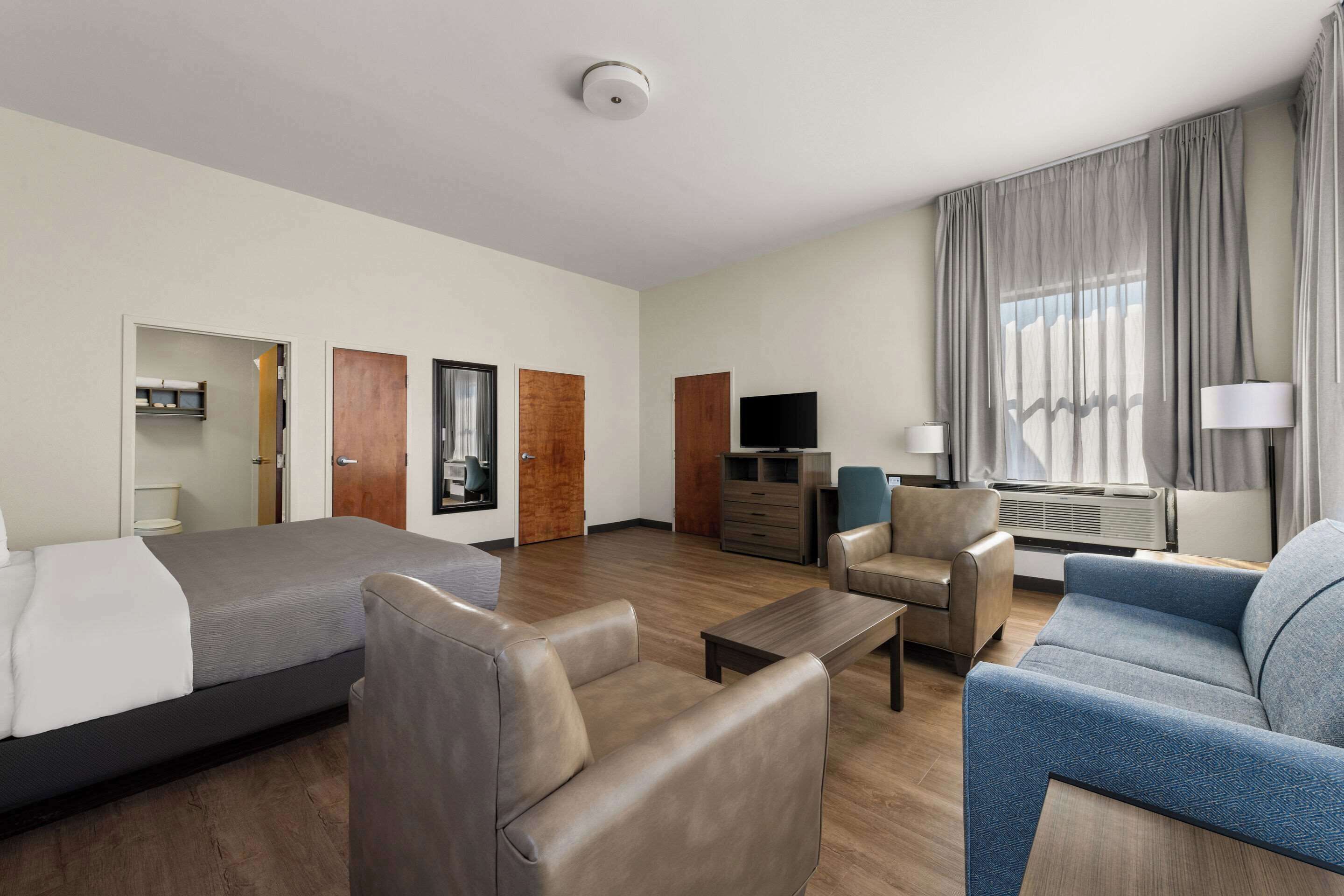 A hotel room with a bed, two sofas, a desk, a TV, and a window with curtains.
