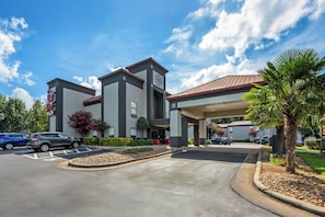 A modern hotel with a covered entrance, a parking lot, and a landscaped area with palm trees. - Red Roof Inn PLUS+ Henderson (Henderson)