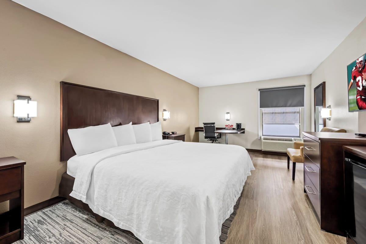 Quarto de hotel com uma cama grande, uma escrivaninha, uma cadeira, uma televisão e uma janela.