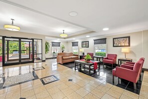 A spacious lobby with a brown leather sofa, red armchairs, a coffee table, and a potted plant. - Red Roof Inn PLUS+ Henderson (Henderson)