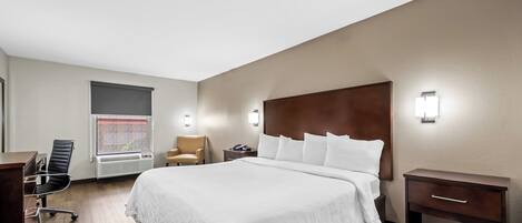 Une chambre d’hôtel avec un grand lit, un bureau, une chaise, une table de chevet et une fenêtre avec des stores.