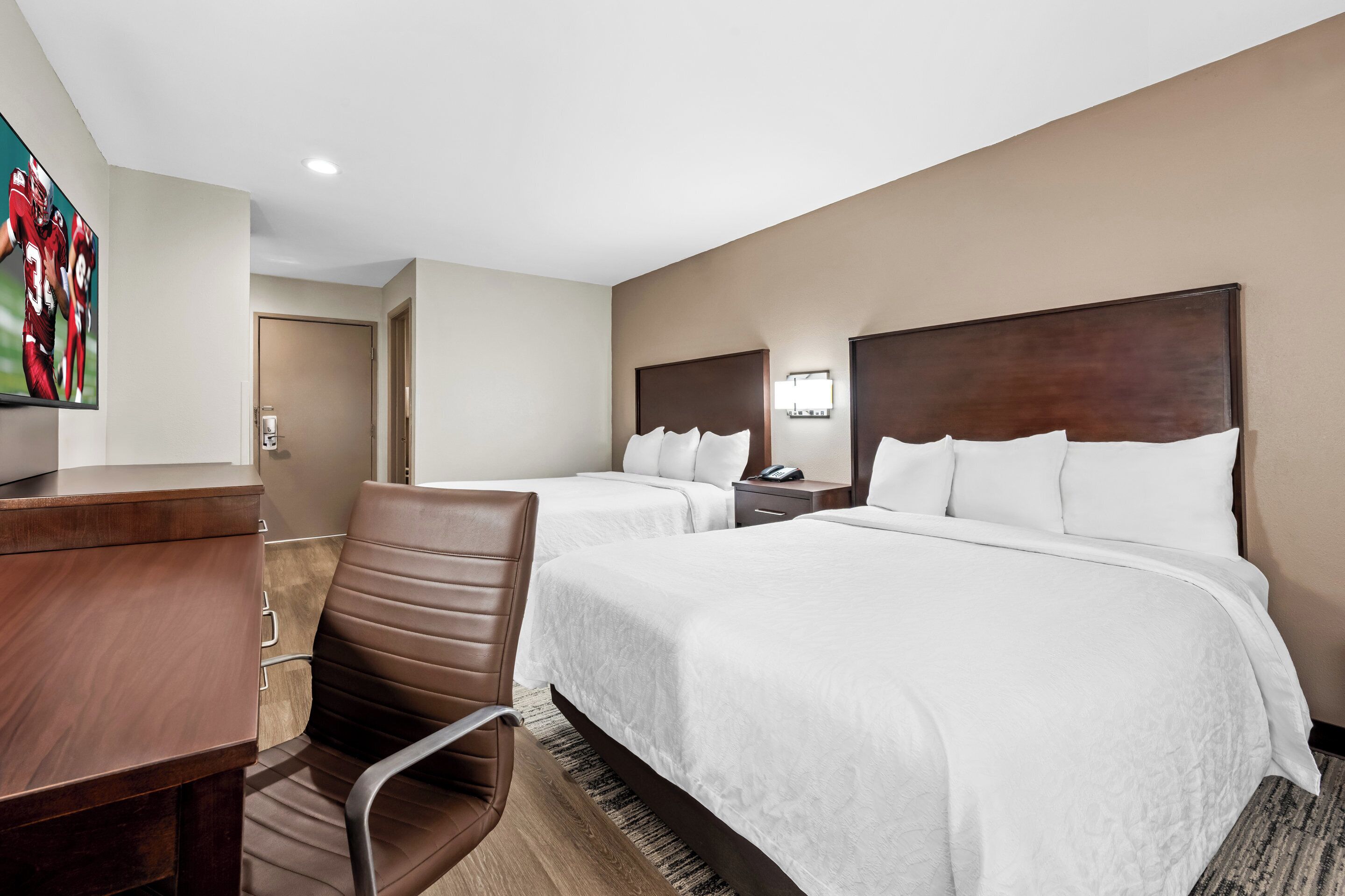 A hotel room with two beds, a desk, a chair, and a TV.