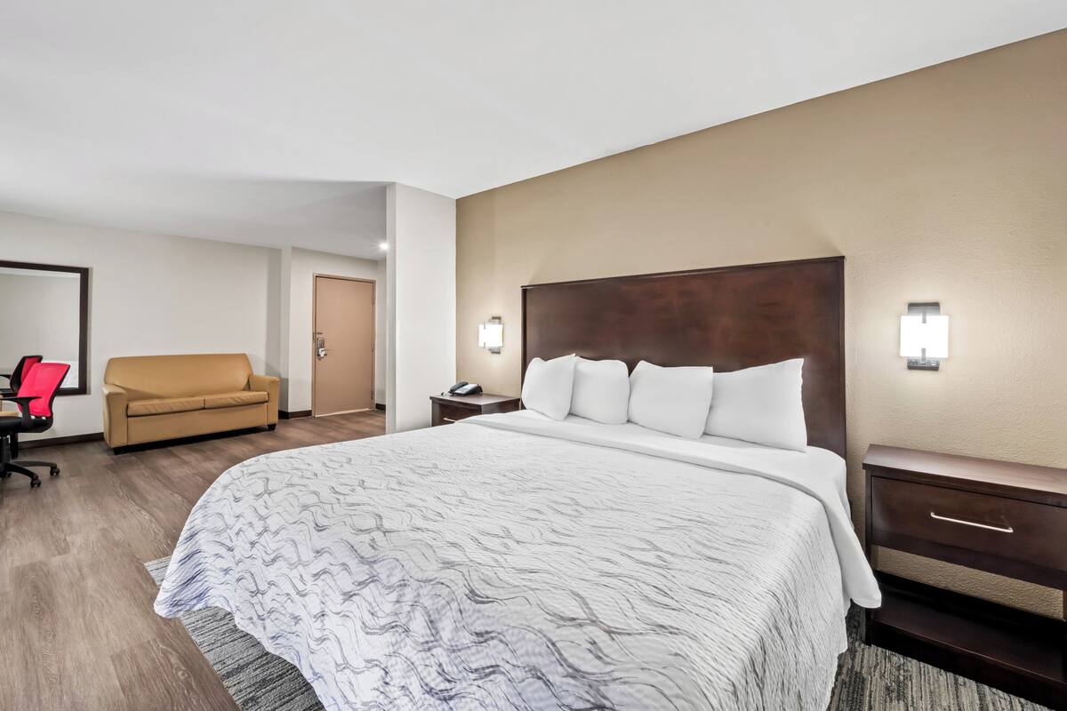 Quarto de hotel com uma cama grande, um sofá, uma escrivaninha e uma cadeira.