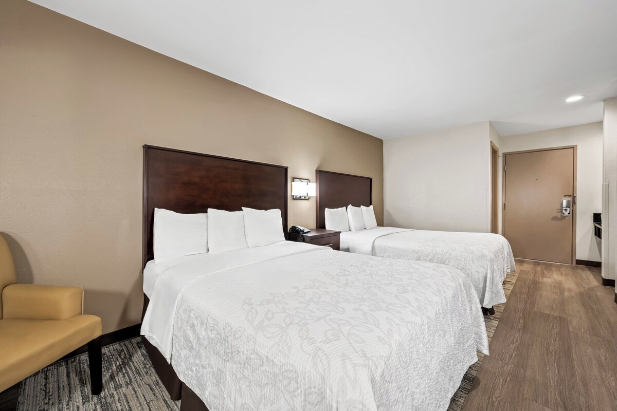 Une chambre d’hôtel avec deux lits, une chaise, un bureau et une porte.