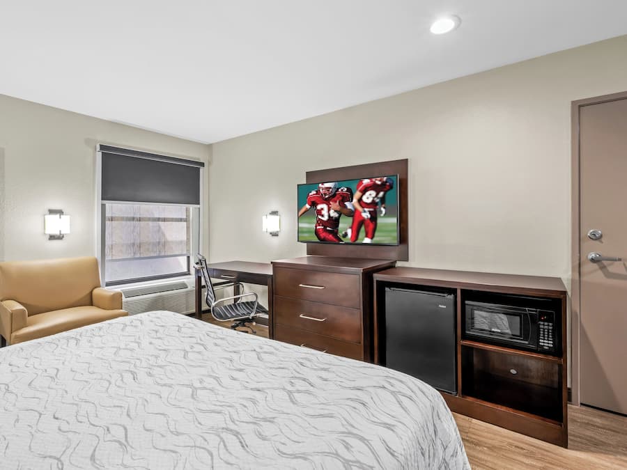 A hotel room with a bed, a desk with a chair, a television, a microwave, and a minibar.