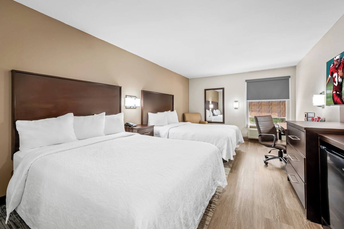 Quarto de hotel com duas camas, uma escrivaninha, uma cadeira e uma televisão.