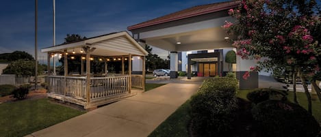 A building with a covered outdoor area, a flag, and well-maintained landscaping.