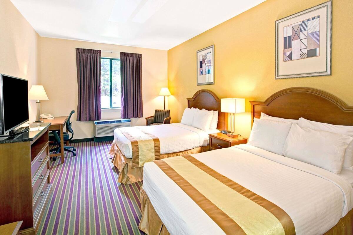 A hotel room with two beds, a desk with a computer, a TV, and a window with curtains.