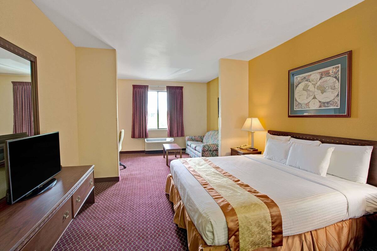 A hotel room with a large bed, a television, a desk, and a window with curtains.