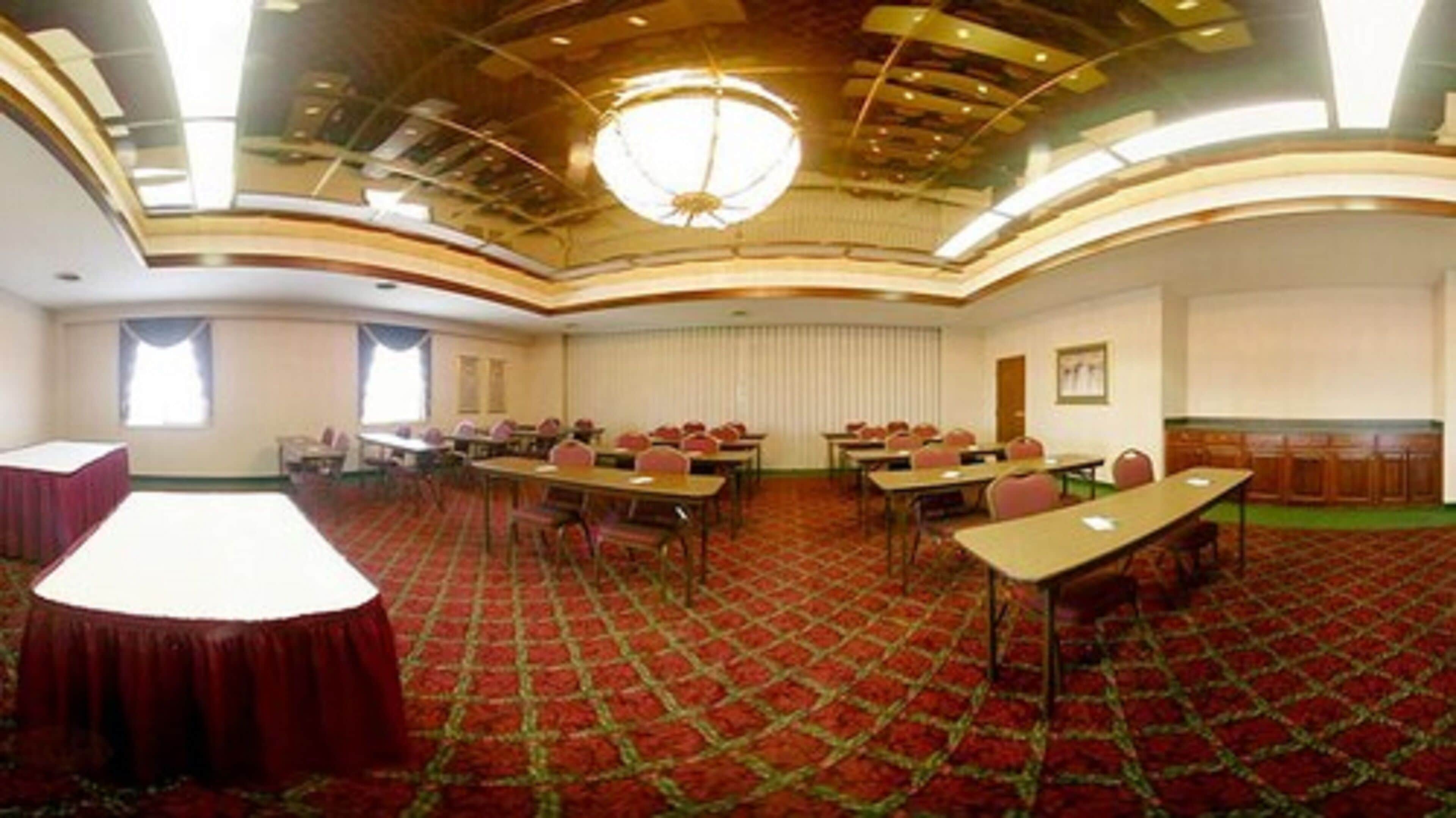 A conference room with a red carpet, tables, chairs, and a chandelier.