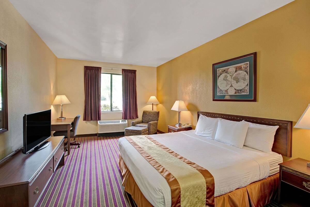 A hotel room with a bed, desk, television, and two lamps.