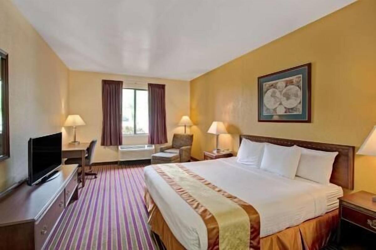 A hotel room with a bed, two bedside tables, a desk with a chair, a television, and a window with curtains.