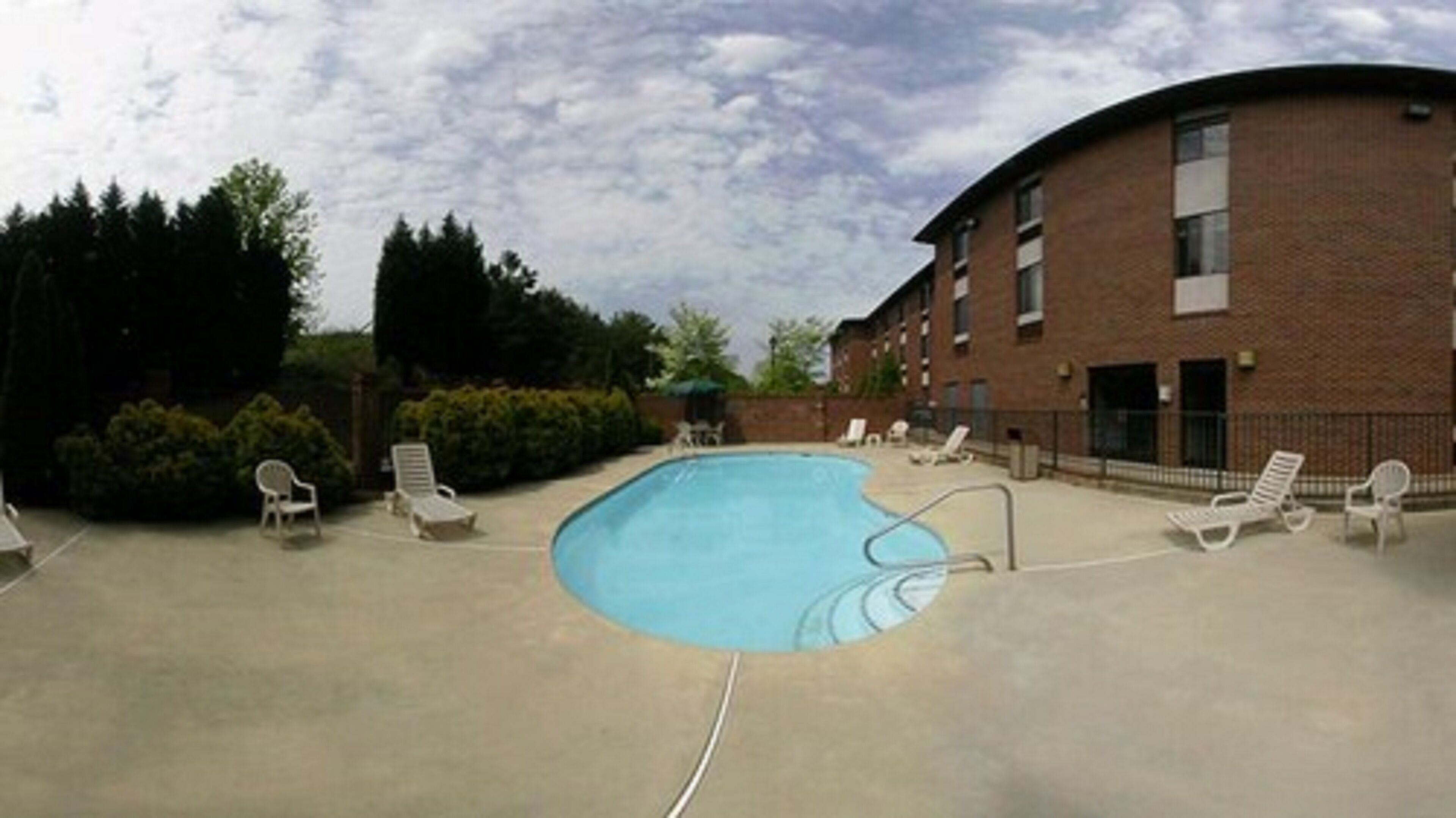 A swimming pool with lounge chairs around it, a brick building, and some trees in the background.