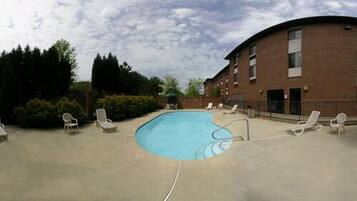 A swimming pool with lounge chairs around it, a brick building, and some trees in the background.