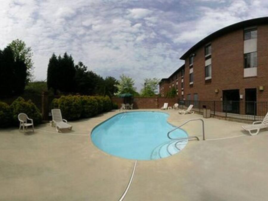 A swimming pool with lounge chairs around it, a brick building, and some trees in the background.
