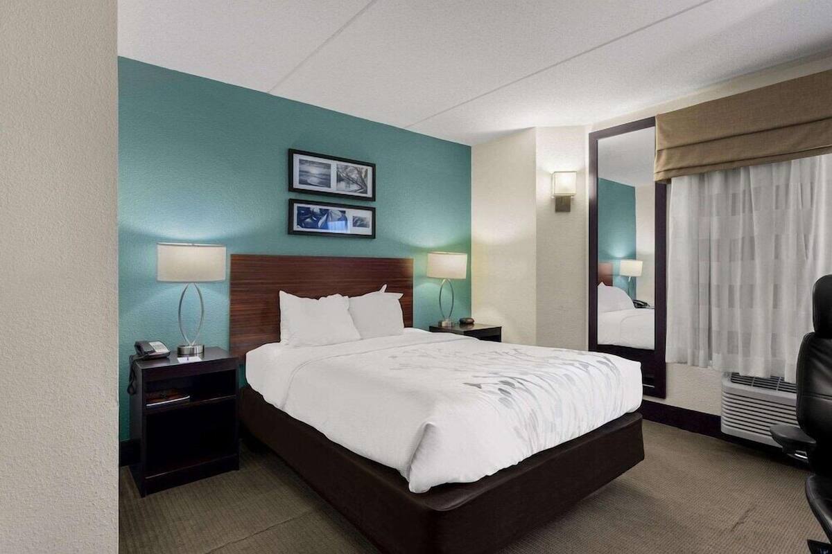 Ein Hotelzimmer mit Bett, Nachttischen, Lampen, einem Spiegel und Blick ins Freie.