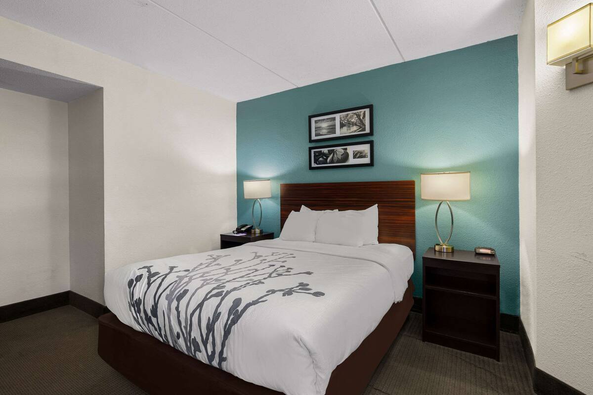 Ein Hotelzimmer mit einem großen Bett, zwei Nachttischen, einem Beistelltisch, einem Holzkopfstück und zwei Wandlampen.
