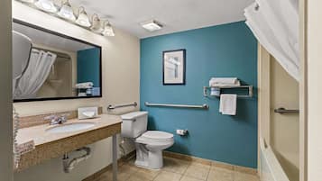 A bathroom with a sink, toilet, and shower. It has a blue wall, a mirror, and a framed picture.