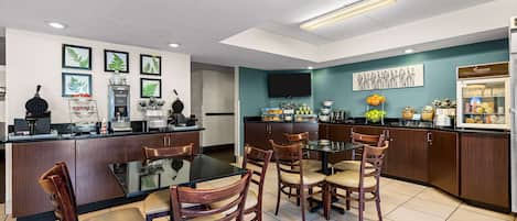 A modern kitchen with a dining area, featuring a central island, wooden chairs, and a flat-screen TV mounted on the wall.