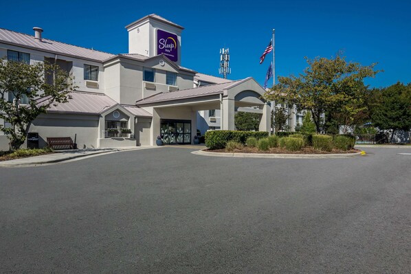 A Sleep Inn hotel with a modern design, featuring a prominent entrance, a parking lot, and a clear blue sky. - Sleep Inn Wilmington near University (Wilmington)