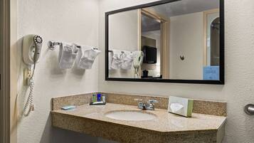 A bathroom with a granite countertop sink, a mirror, a hairdryer, and a towel rack.
