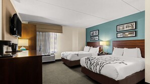 A hotel room with two beds, a desk with a coffee maker, a TV, and framed pictures on the wall. - Sleep Inn Wilmington near University (Wilmington)