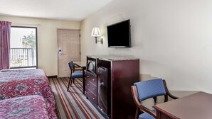 Ein Hotelzimmer mit zwei Betten, einem Schreibtisch, einem Sessel, einem Fernseher und einem Fenster mit Vorhängen.