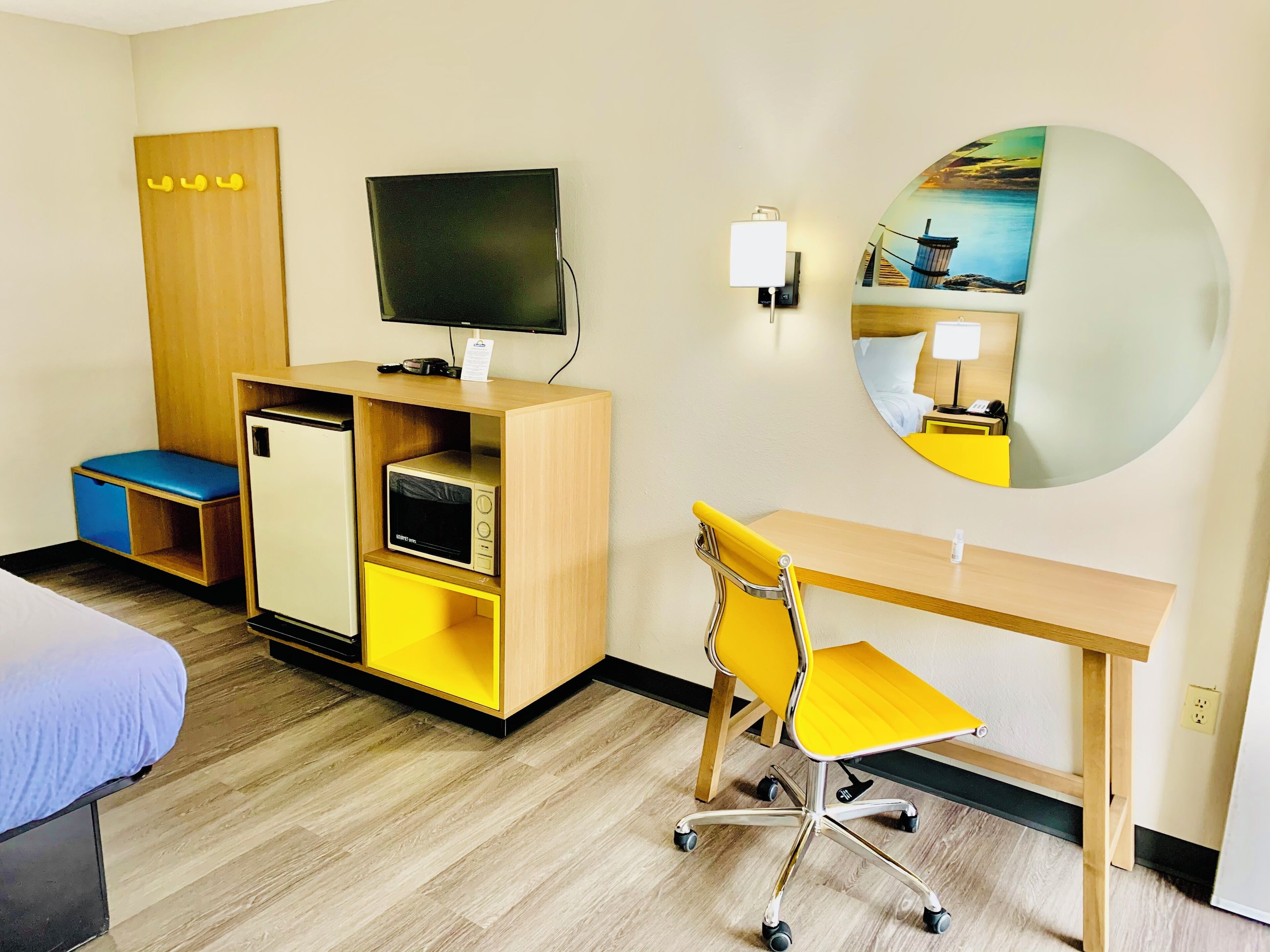 Ein Hotelzimmer mit einem Bett, einem Schreibtisch mit Stuhl, einem Fernseher, einer kleinen Kühlbox, einem Spiegel und einem Holzschrank.