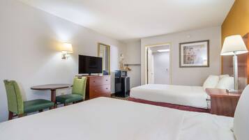 Quarto de hotel com cama, escrivaninha e cadeira, televisão, cômoda e uma mesinha.