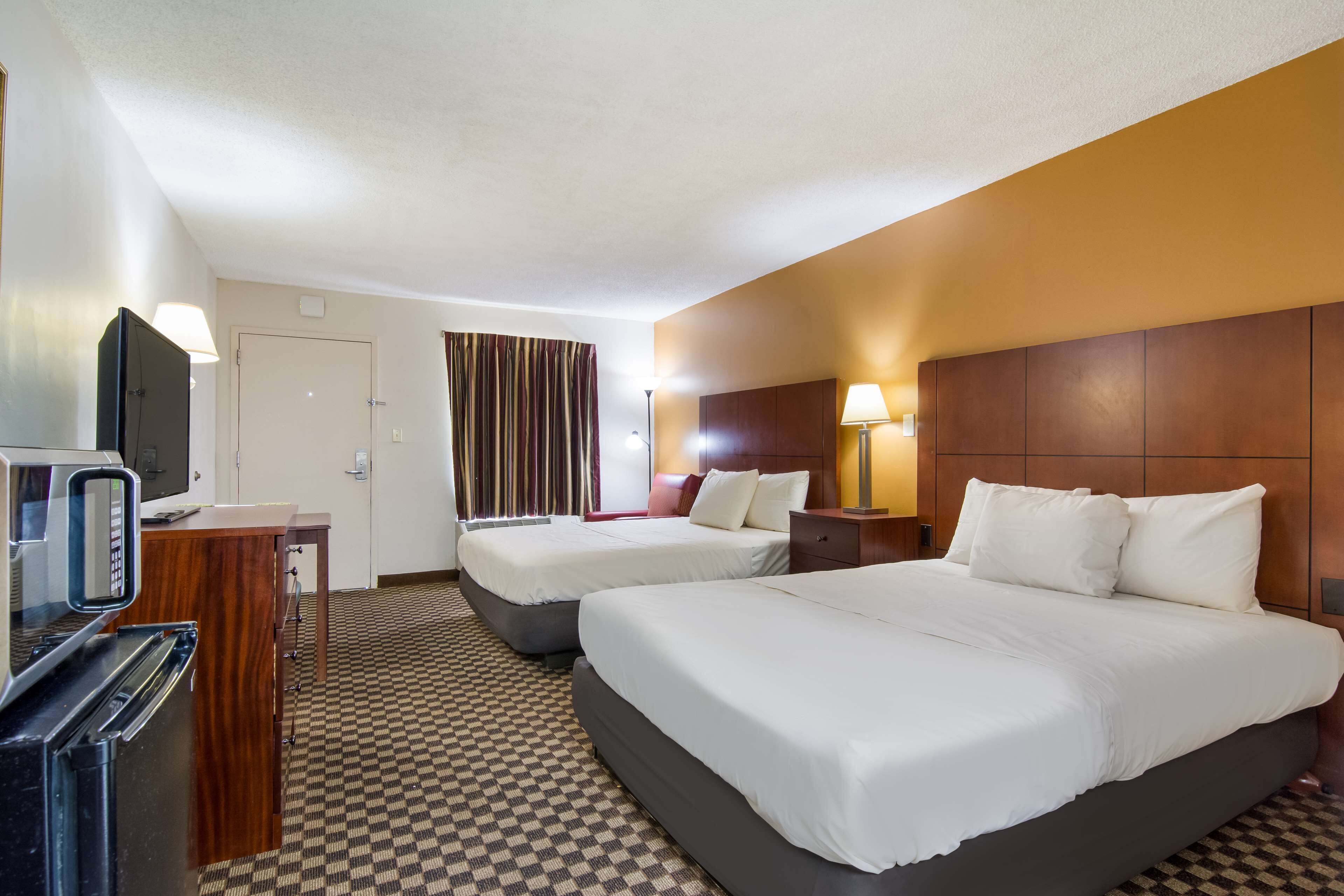 A hotel room with two beds, a desk with a television, and a check-in counter.