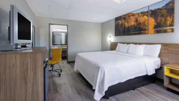 A hotel room with a bed, a desk with a computer, a chair, a mirror, and a painting on the wall. - Days Inn by Wyndham Lincolnton (Lincolnton)