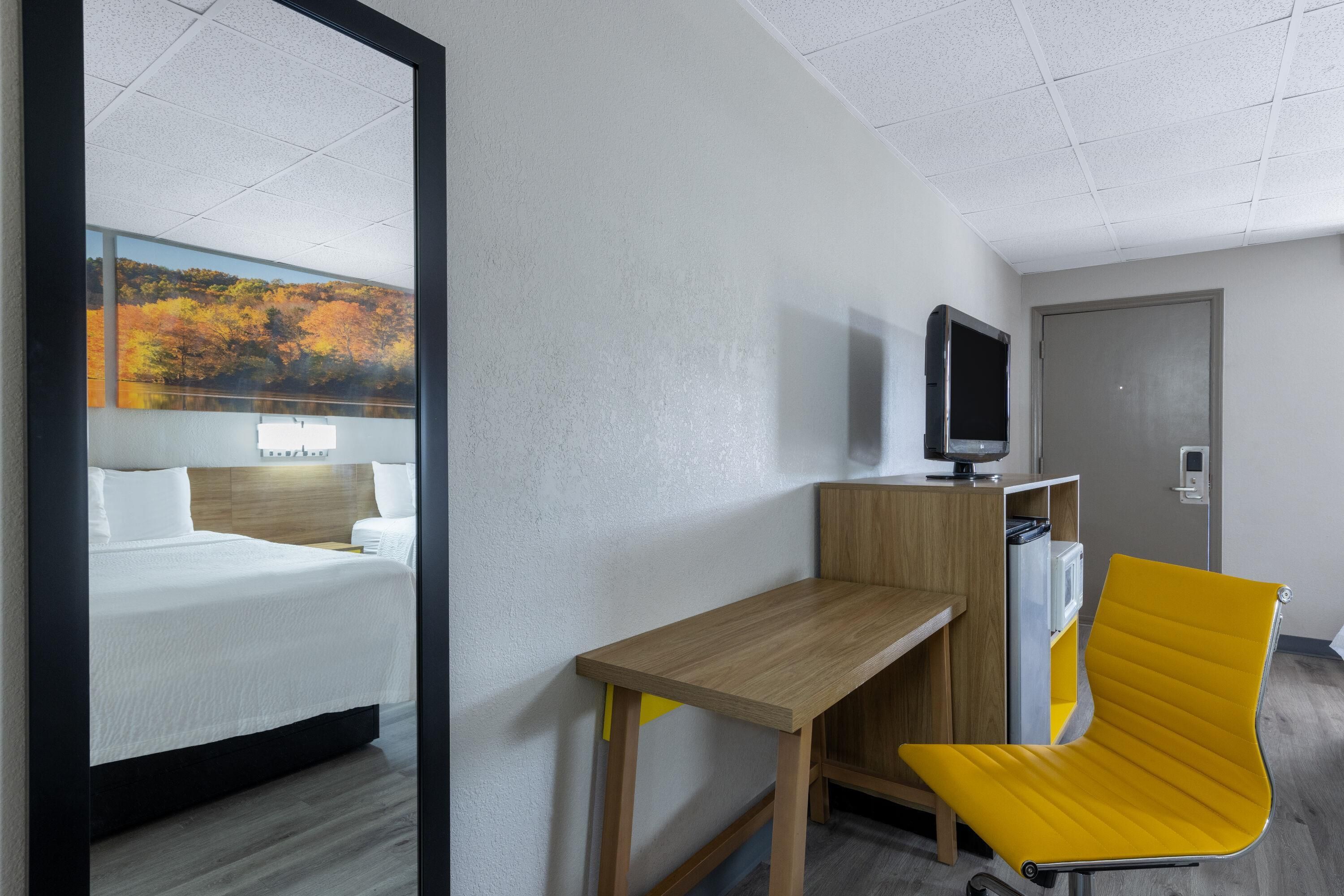 A hotel room with a bed, a desk, a chair, a television, and a door.