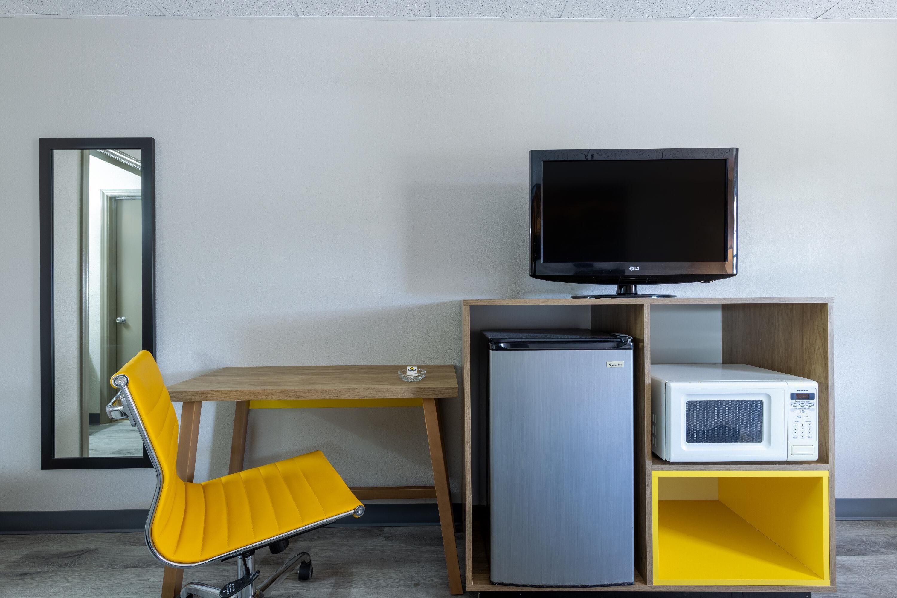 A compact room with a wooden desk, a yellow chair, a television, a refrigerator, and a microwave.