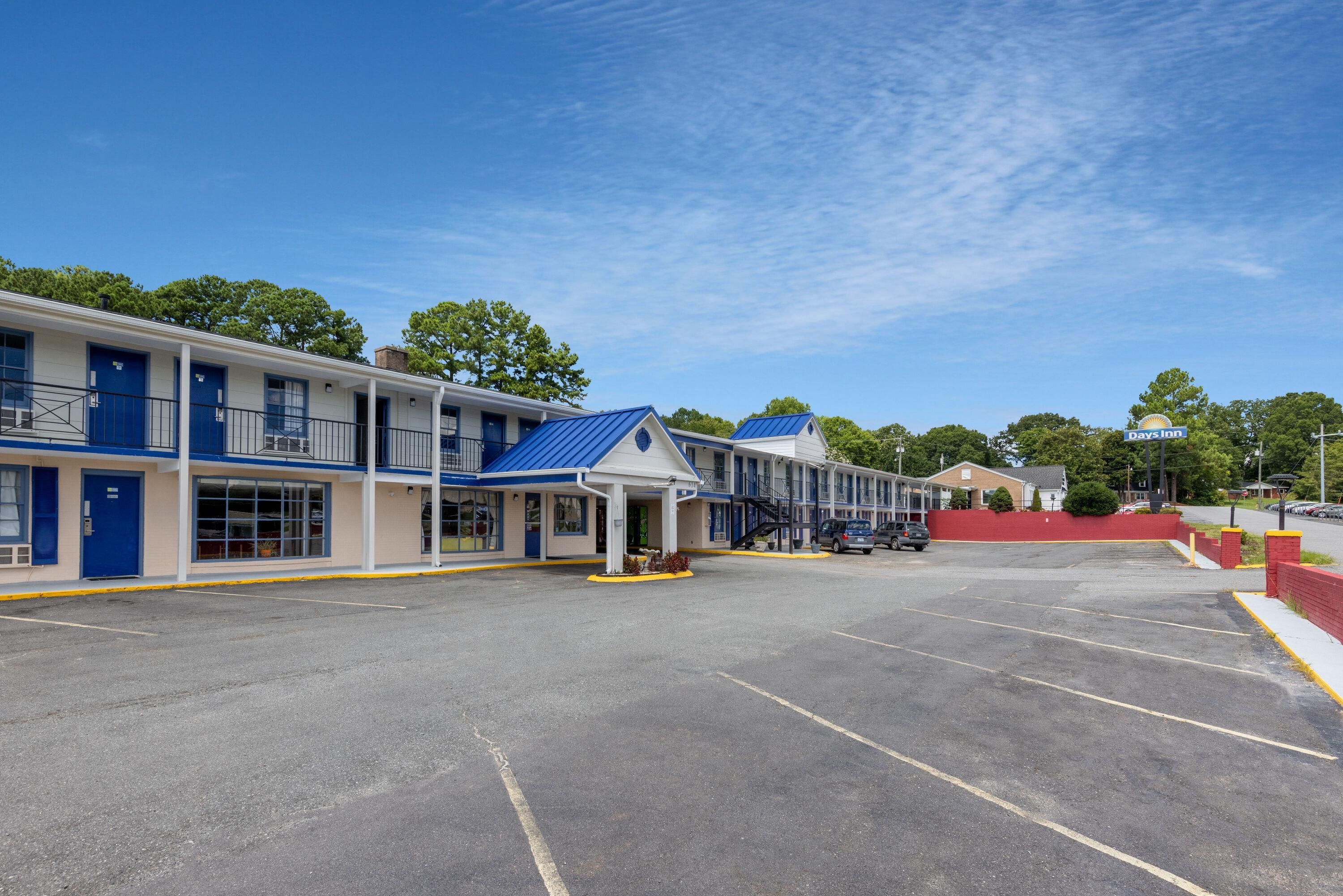 Un motel con varias habitaciones, zona de estacionamiento techada y cielo despejado.