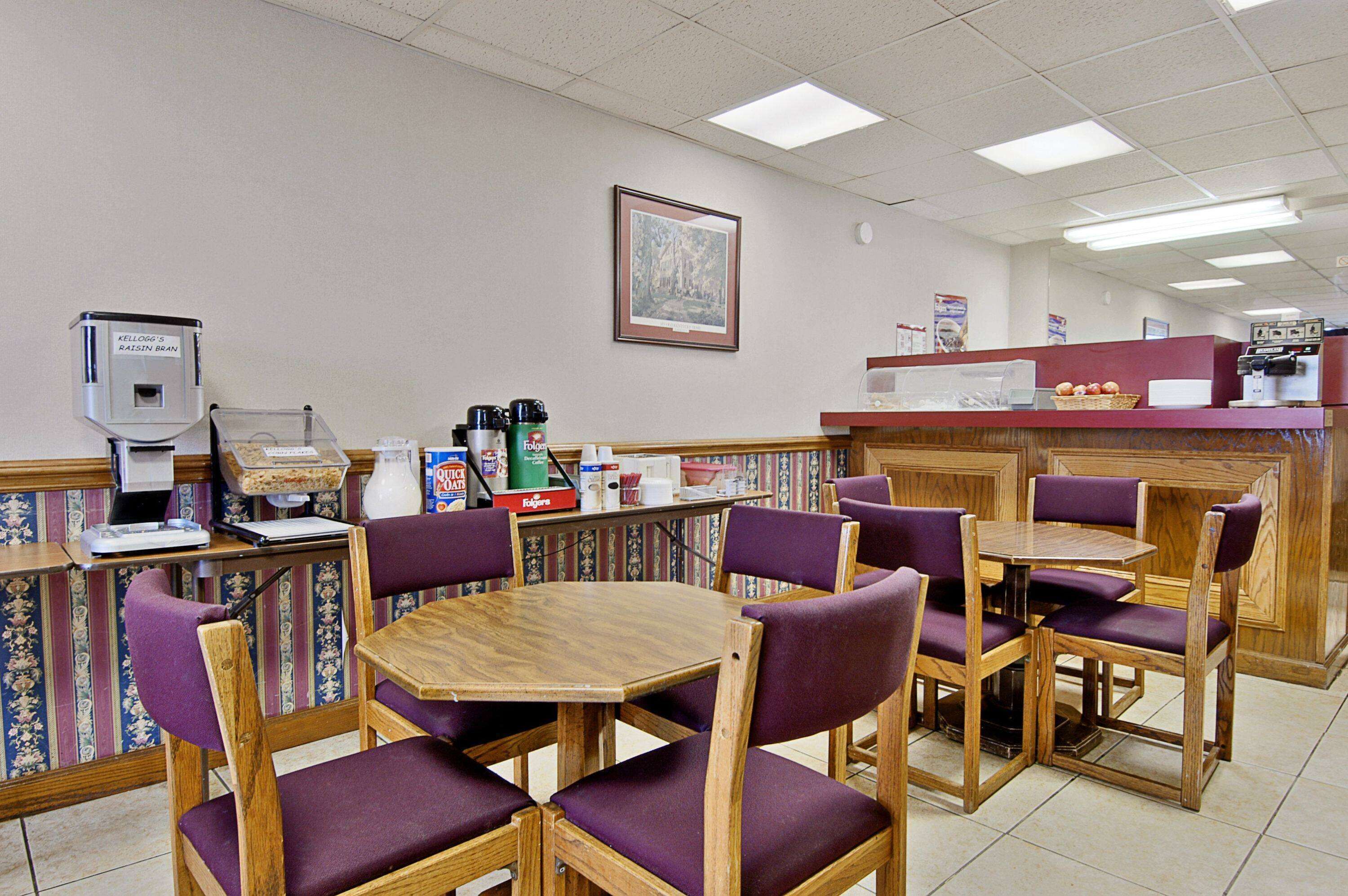 A restaurant with wooden tables and purple chairs, a coffee machine, and a cash register.